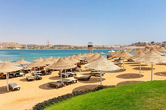 Sandy beach with straw umbrellas, sun loungers, and clear blue sea under a sunny sky
