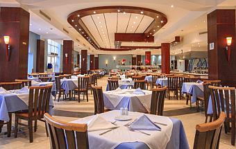 Spacious dining hall with wooden chairs, blue tablecloths, and ceiling lights