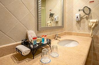 Bathroom countertop with sink, toiletries, and mirror in a tiled setting