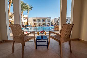 Patio with two wicker chairs and small table overlooking pool and resort buildings