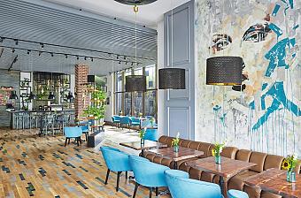 Modern hotel lounge with teal chairs, bar counter, pendant lights, and mural wall for training camp downtime