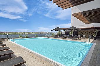 Outdoor pool with loungers and umbrellas overlooking a river—training camp recovery and cooldown area
