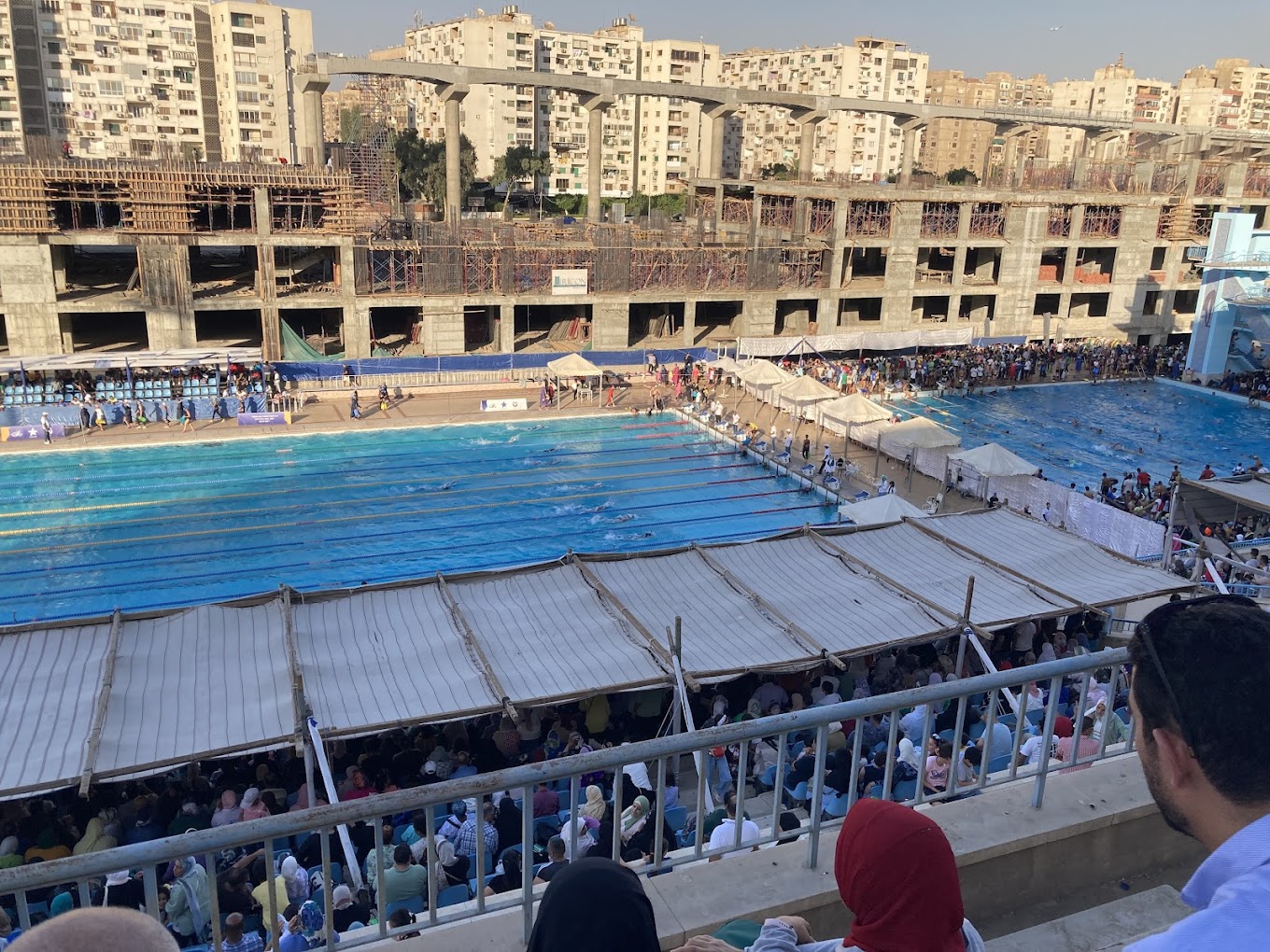 Volles Außen-Schwimmmeeting mit Zelten am Beckenrand und Zuschauern auf den Tribünen.