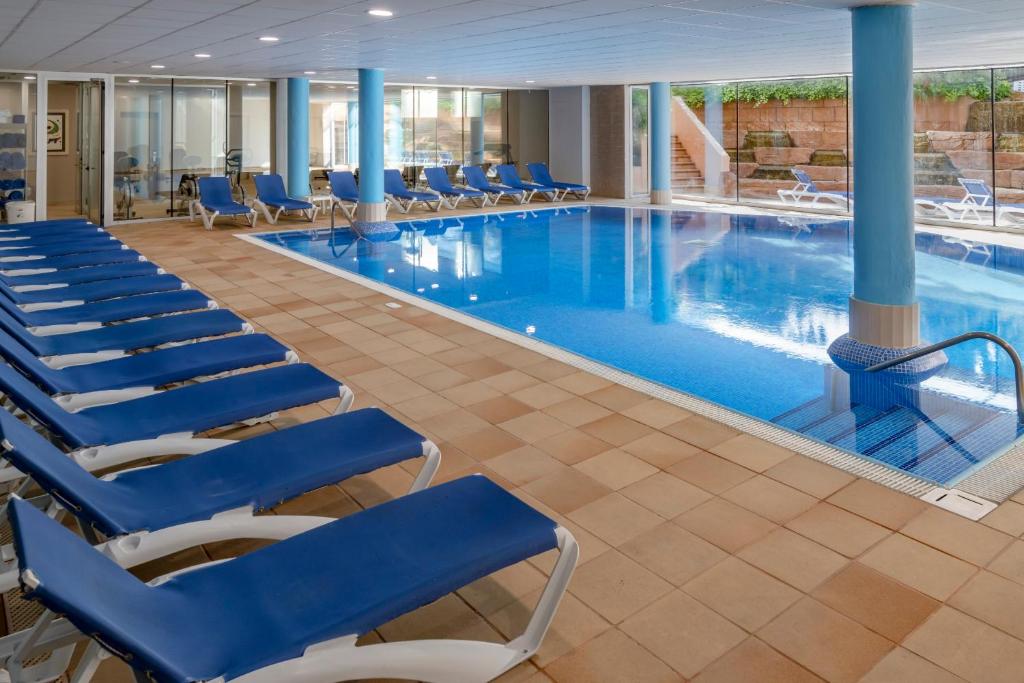 Hallenbad mit gefliestem Bereich und blauen Liegen entlang des Beckens.