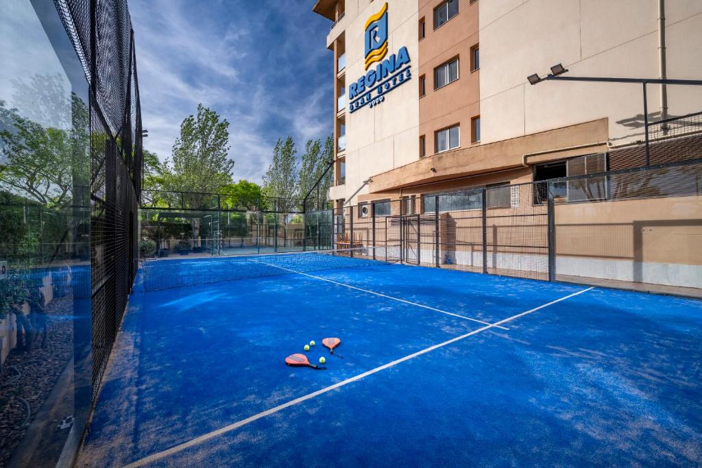 Padelplatz im Freien mit Netz, Schlägern und Bällen auf dem Belag neben dem Hotelgebäude.