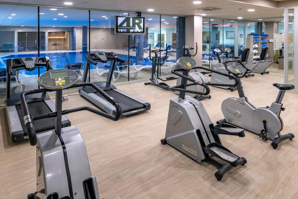 Fitnessraum mit Cardiogeräten (Laufbänder und Fahrräder) und Glasfront mit Blick auf den Innenpool.