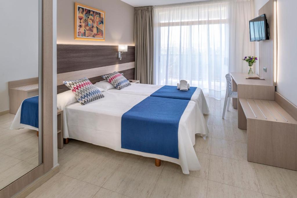 Helles Zweibettzimmer mit zwei Einzelbetten, Wand-TV, Schreibtisch und großem Balkonfenster.