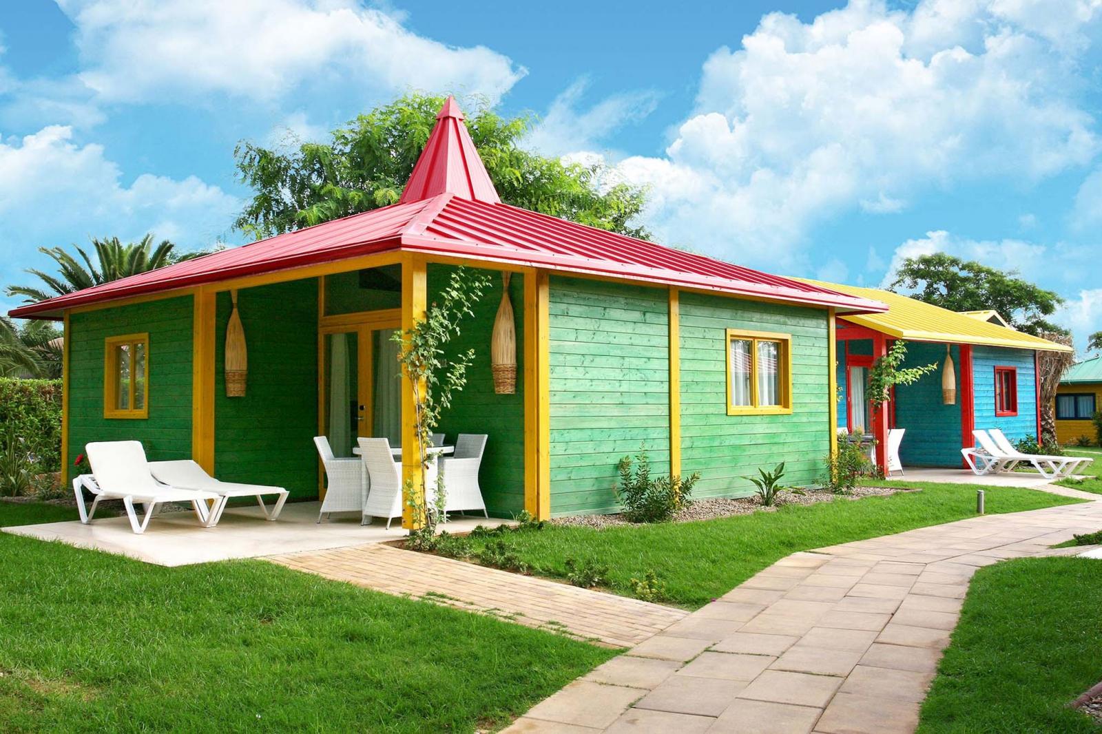 Extérieur de cottage coloré avec salon de terrasse et chaises longues le long d'une allée pavée.