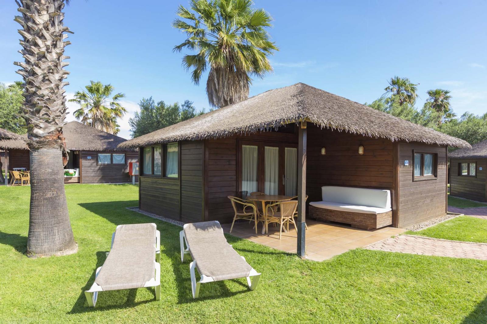 Bungalow en bois avec terrasse couverte et chaises longues sur une pelouse.