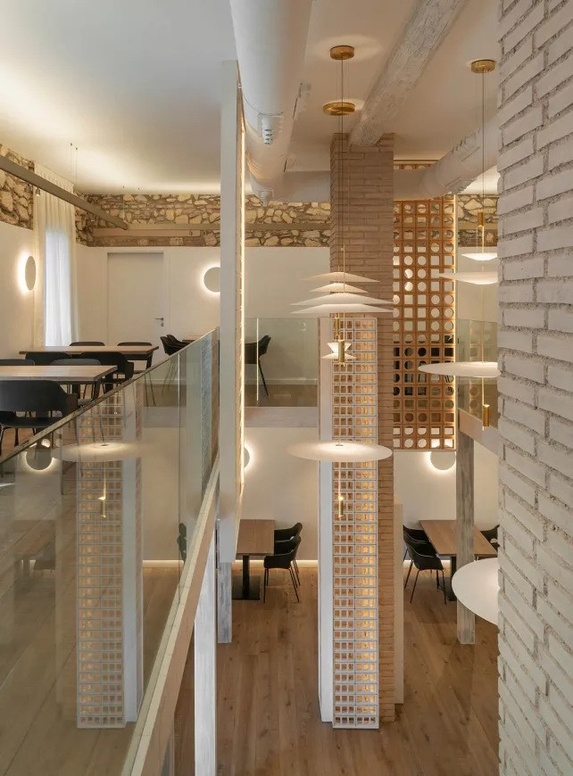 Espace restauration intérieur sur deux niveaux avec tables, garde-corps en verre et suspensions modernes.
