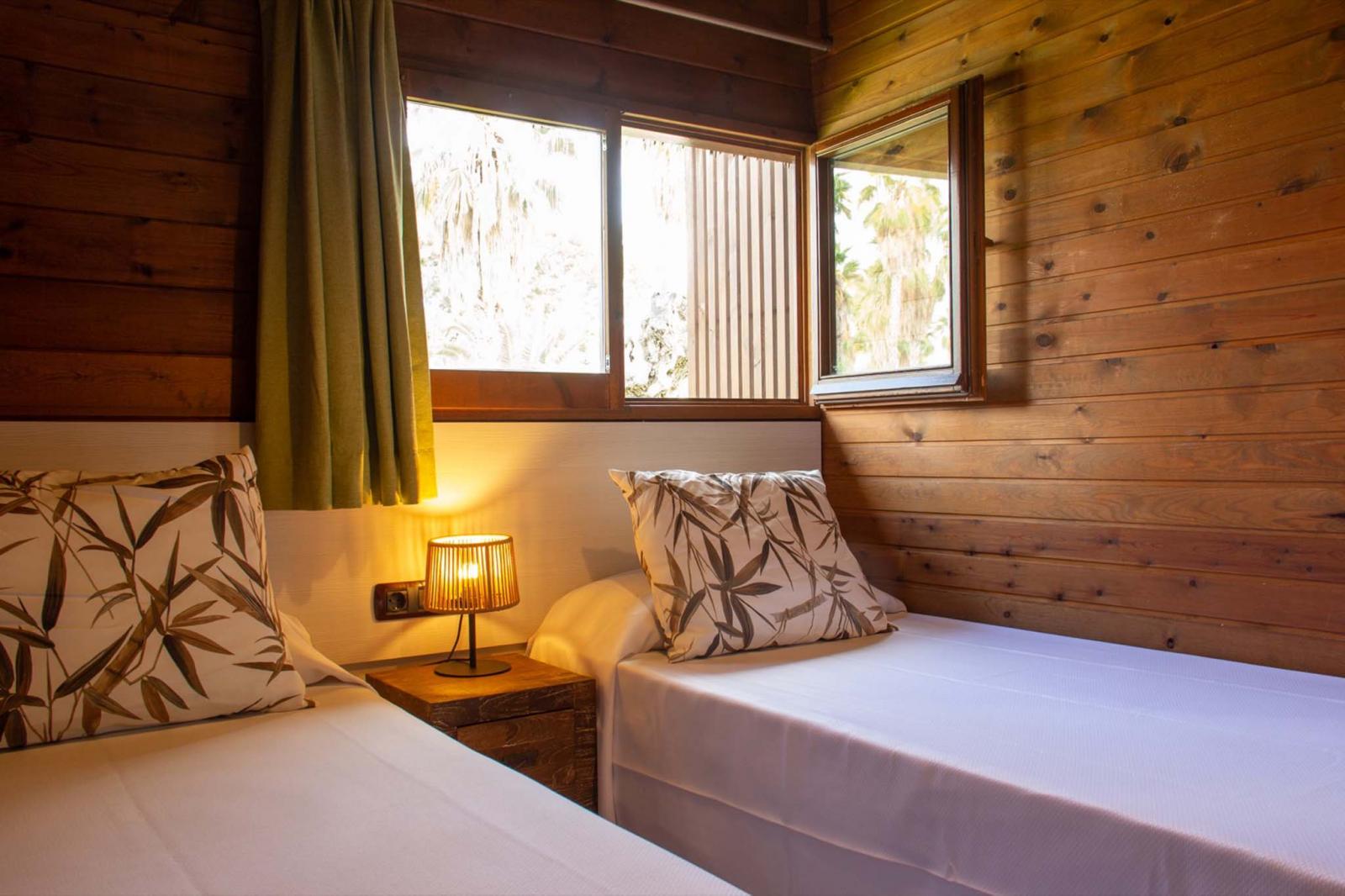 Chambre twin avec murs lambrissés en bois, lampe de chevet et fenêtre.