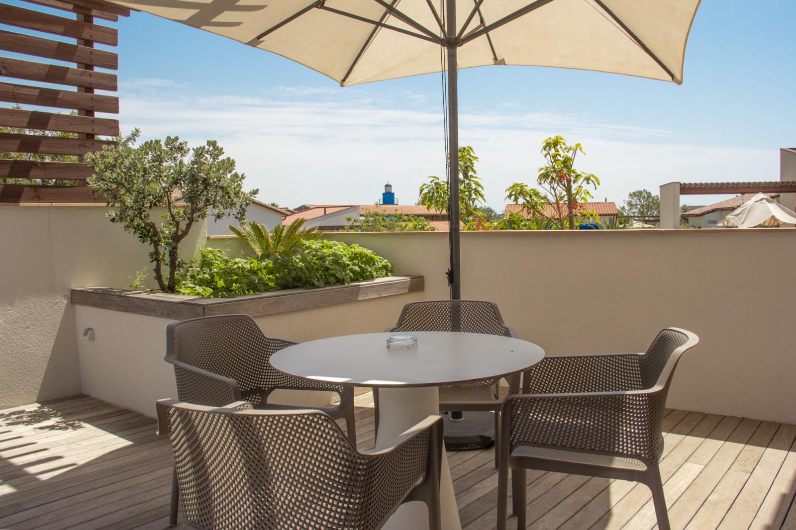 Terrasse extérieure avec table ronde, chaises et grand parasol surplombant les toits.