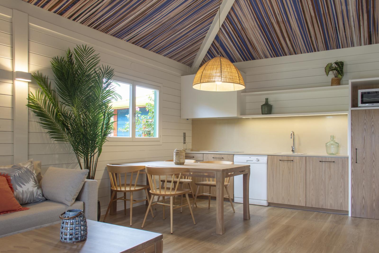 Coin salon du bungalow avec canapé, table à manger et kitchenette sous un plafond à rayures.
