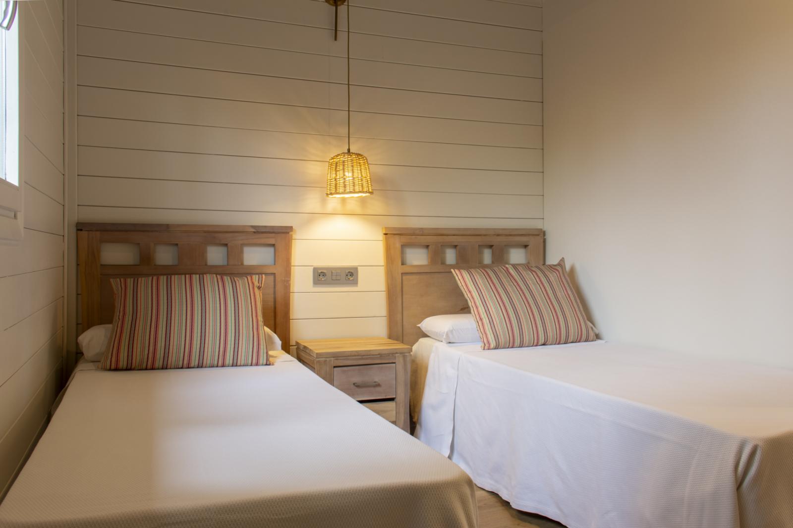 Chambre twin lumineuse avec deux lits simples, table de chevet et lampe suspendue.