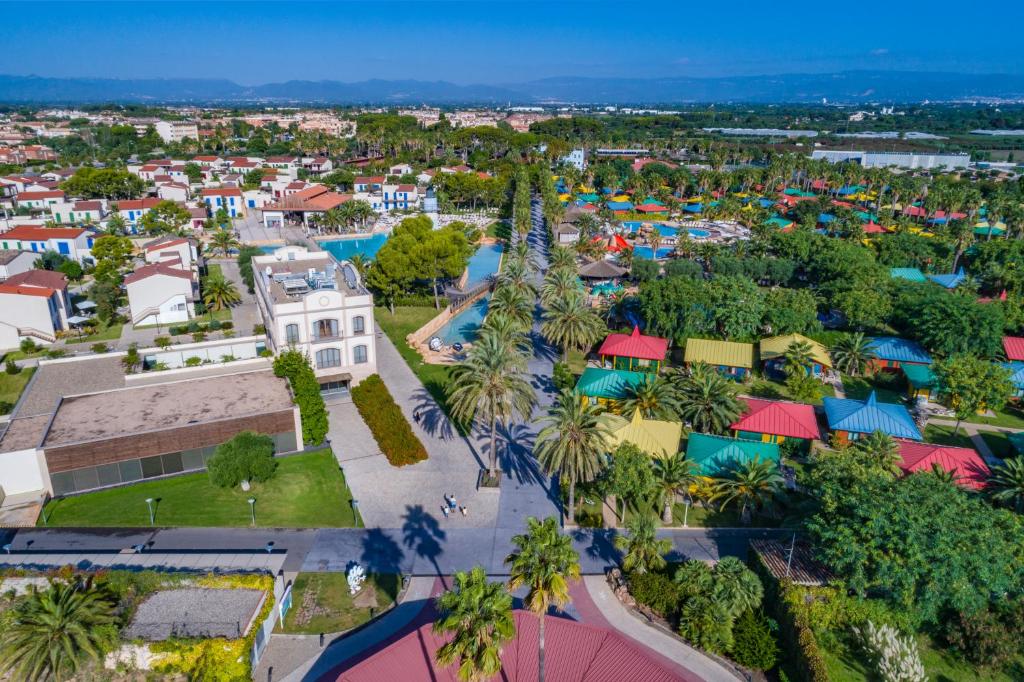 Vue aérienne du complexe avec allées bordées de palmiers, piscines et bungalows colorés.