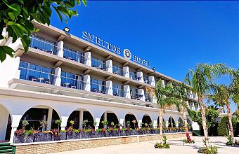Front exterior of the hotel building with balconies and palm trees.