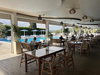 Covered restaurant terrace beside the outdoor pool with tables and seated guests.