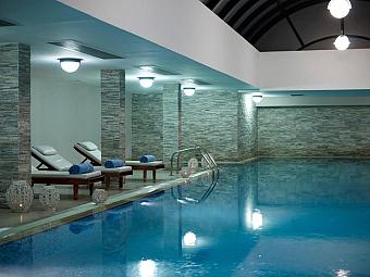 Indoor spa pool with loungers, towels and stone walls.