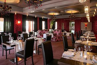 Restaurant dining room with set tables, chandeliers and patterned seating.