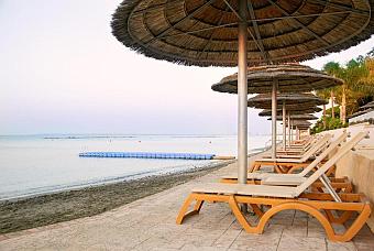 Beachfront sun loungers under parasols beside calm sea and floating dock.