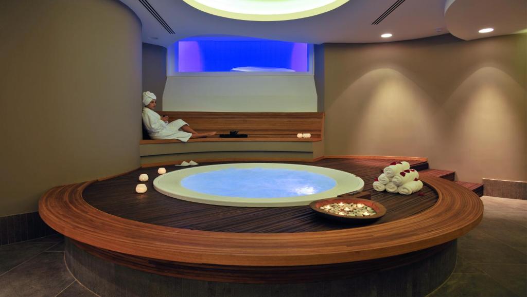 Spa room with round jacuzzi, candles, towels and a seated guest.