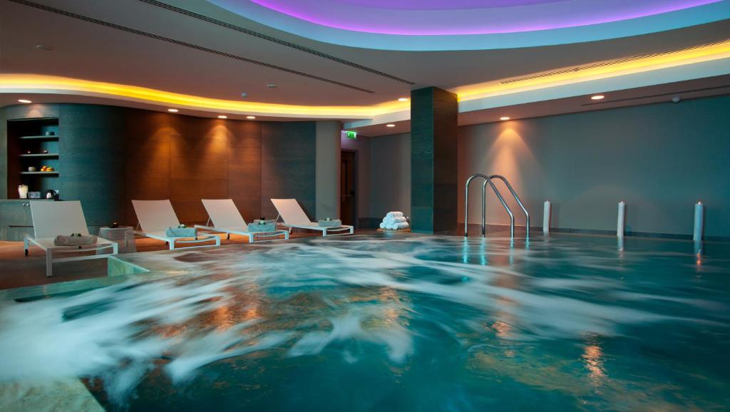 Indoor hydrotherapy pool with loungers and ambient ceiling lighting.
