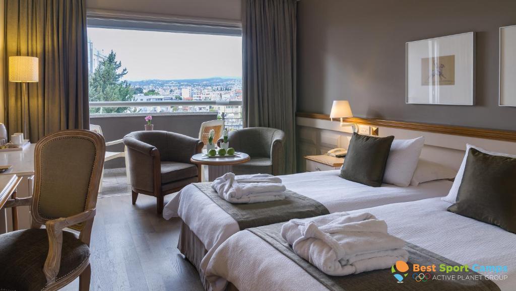 Twin guest room with balcony view, desk and armchairs.