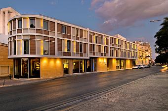 Modern hotel exterior on a city street at dusk with illuminated facade and entrance.
