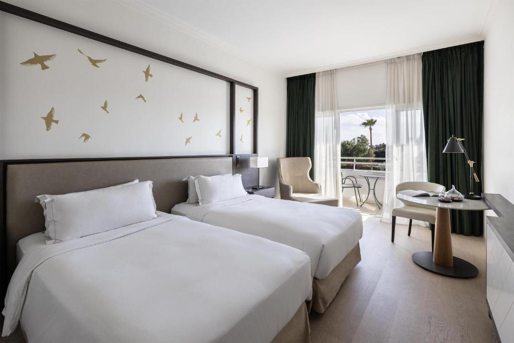 Twin guest room with balcony seating, desk and garden view.