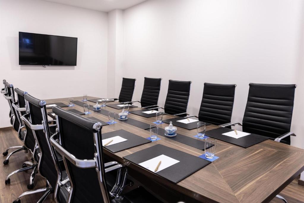 Boardroom with leather chairs, notepads, water glasses and a wall-mounted screen.