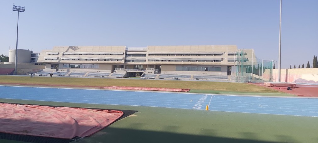 Weitwinkelansicht eines Sportkomplexes mit blauen und roten Laufbahnen sowie zentralem Rasenfeld
