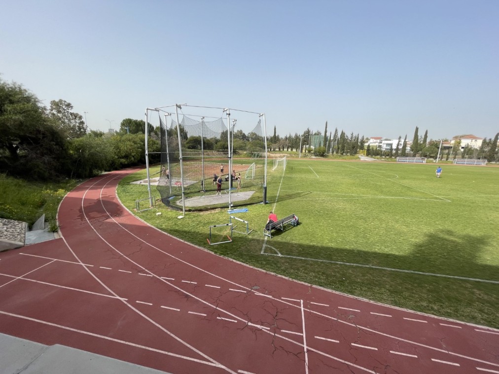 Leichtathletikfeld mit Wurfkäfig, Laufbahnen und grünem Trainingsbereich für Technikübungen in Wurfdisziplinen