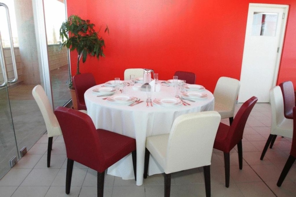 Runder Esstisch mit weißer Tischdecke, roten und weißen Stühlen vor einer hellroten Wand