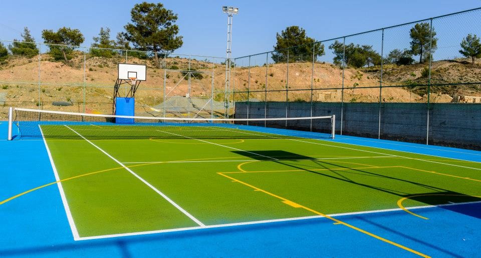 Kombination aus Tennis- und Basketballplatz mit grünen und blauen Spielflächen und Umzäunung