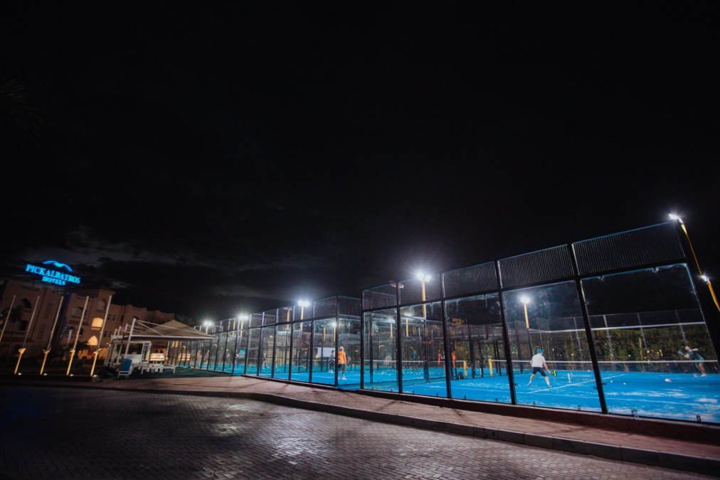 Beleuchtete Outdoor-Padelplätze neben dem Hotel bei Nacht, mit mehreren spielenden Personen.