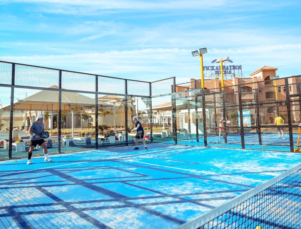 Personen spielen tagsüber auf einem blauen Outdoor-Padelplatz neben dem Hotel.