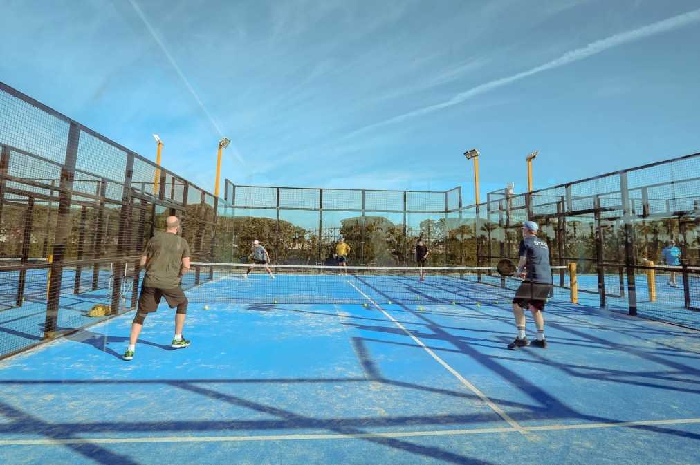 Padel-Einheit auf einem blauen Outdoor-Platz mit mehreren sichtbaren Bällen auf dem Boden.