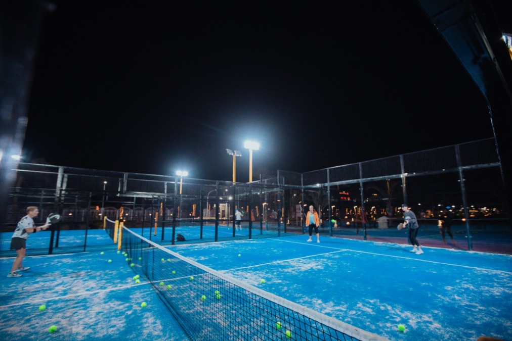 Padel-Doppel auf einem blauen Outdoor-Platz unter Flutlicht bei Nacht.