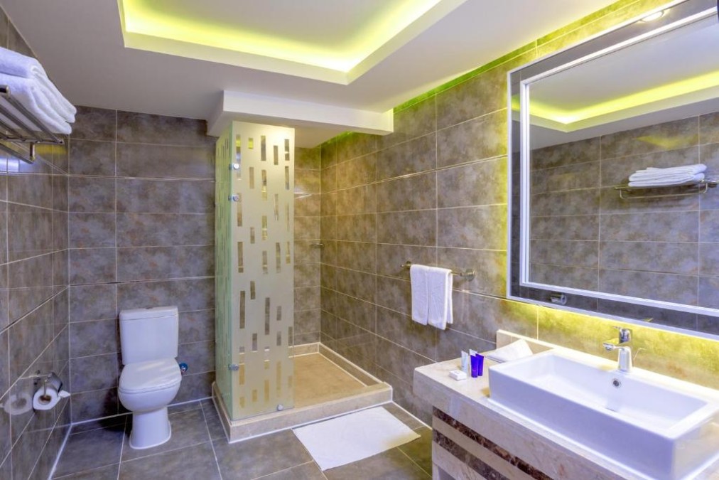 Modernes Badezimmer mit gefliesten Wänden, begehbarer Dusche, Toilette, beleuchtetem Spiegel und Waschbecken mit Ablagefläche