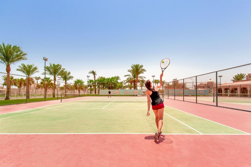 Tennisspielerin beim Aufschlag auf einem Außenplatz mit Palmen