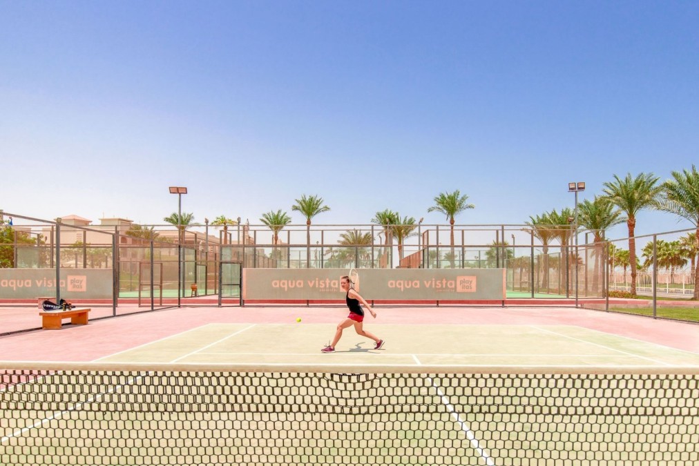 Athlet spielt Tennis auf einem roten und grünen Platz unter klarem blauem Himmel