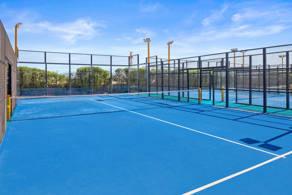 Blauer Padel-Tennisplatz mit Netz und umzäuntem Bereich unter klarem Himmel