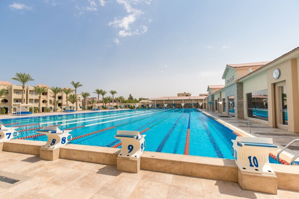 Olympisches Freibad mit Sprungplattformen, umgeben von Palmen und Sporttrainingsanlagen