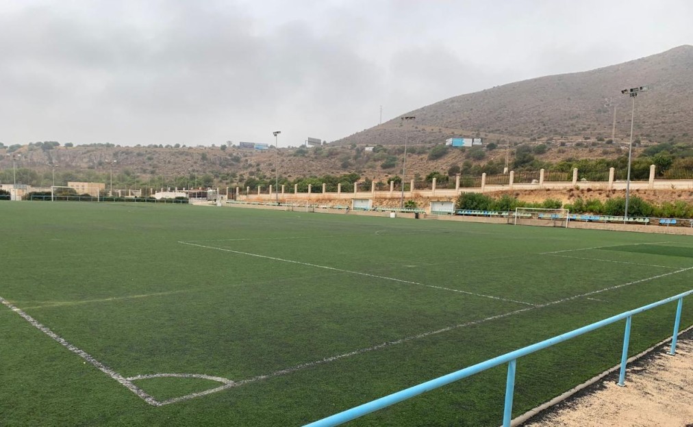 Großes Kunstrasen-Fußballfeld vor hügeliger Kulisse.