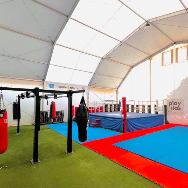 Kampfsport-Zelt mit Boxring, Sandsäcken und Trainingsmatten für Drills.