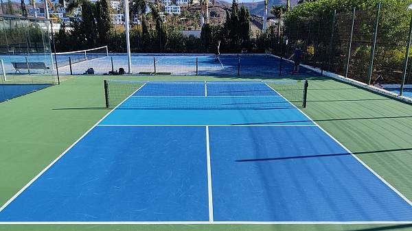 Außen-Tennisplatz mit blauem Hartbelag, Netz und Umzäunung.