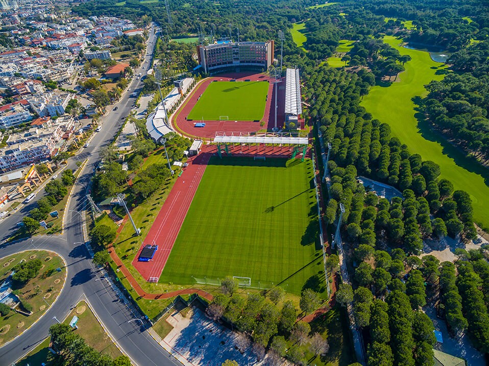Luftaufnahme eines weitläufigen Sportkomplexes mit Stadionanlagen und mehreren Trainingsfeldern in grüner Umgebung. Die Anlage zeigt die Größe und Vielfalt der verfügbaren Venues für Camps und Turniere.
