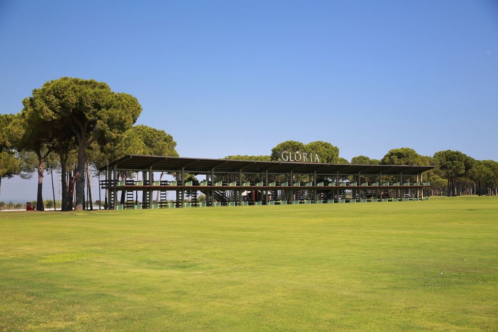 Golf-Driving-Range mit überdachten Abschlagplätzen und weitem Fairway für Long- und Short-Game-Training. Die geschützte Anlage ermöglicht konstantes Üben bei unterschiedlichen Wetterbedingungen.
