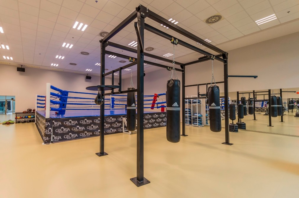 Eigener Boxbereich mit Ring und mehreren hängenden Sandsäcken für Schlagtraining. Die großzügige Trainingsfläche eignet sich für Technikdrills, Kondition und Gruppeneinheiten.