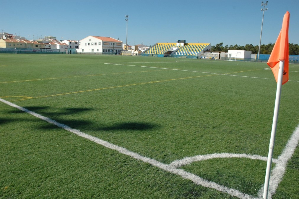 Ecke eines Fußballplatzes mit Kunstrasen und kleiner Tribüne.